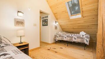 A cozy attic bedroom with a sloped ceiling, a bed with a checkered blanket, a bedside lamp, and a small table.