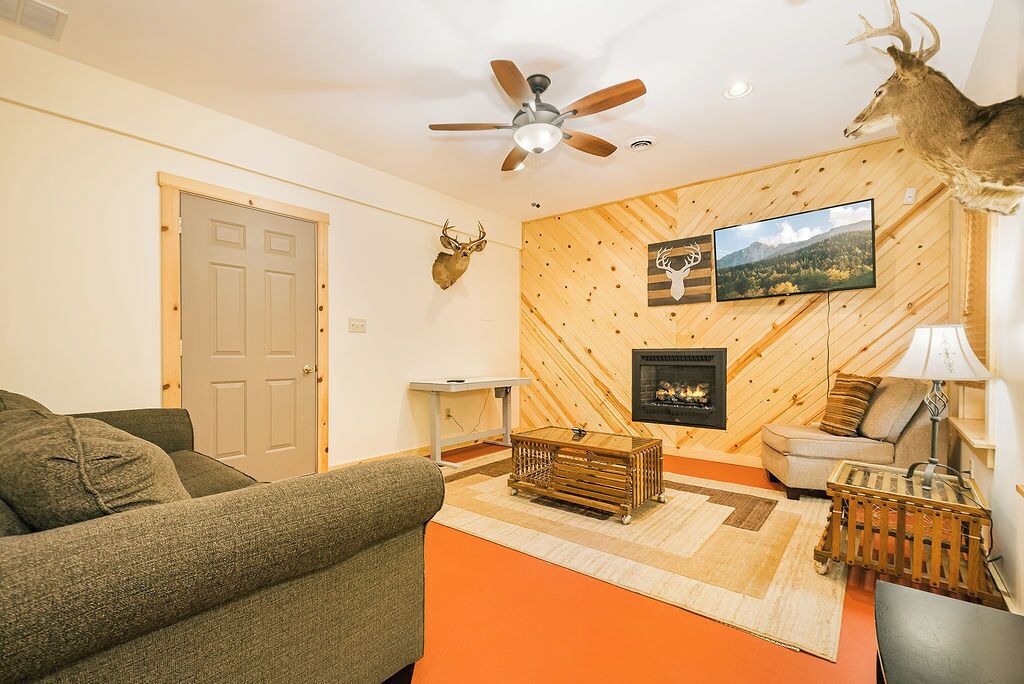 Ein Wohnzimmer mit Holzwand, Deckenventilator, montiertem Hirschgeweih, Kamin und Fernseher.