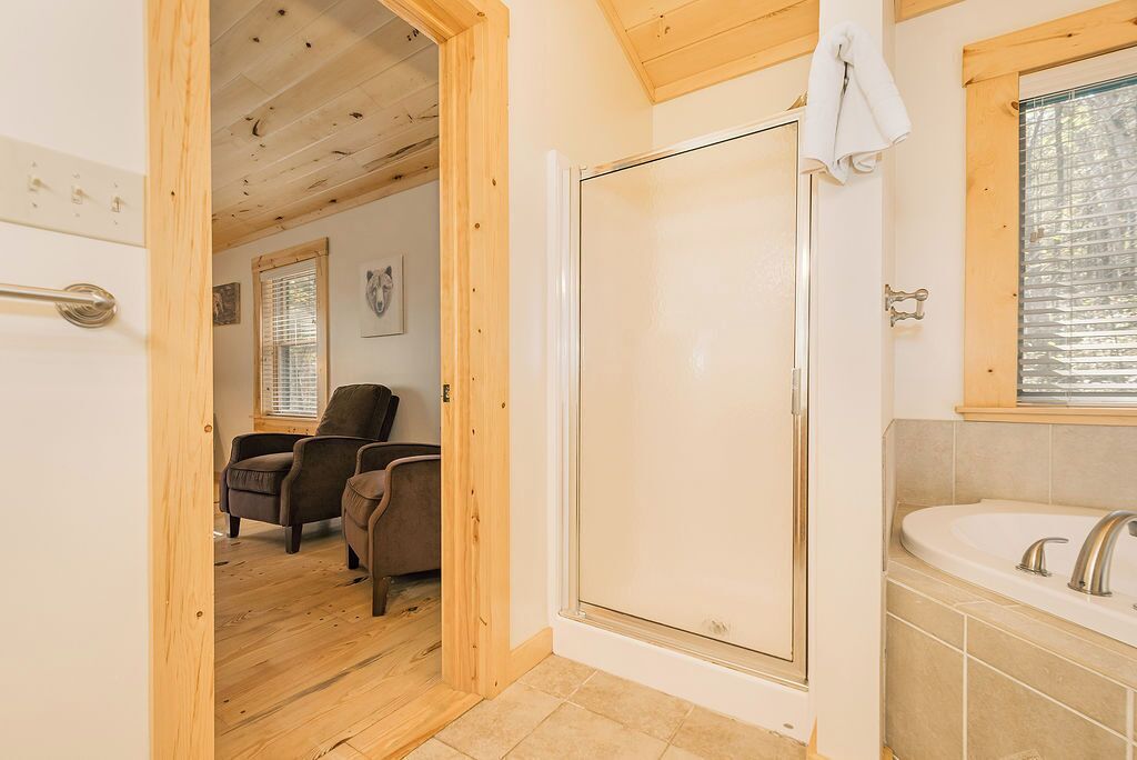 Interior de fusta amb un envàs de dutxa de vidre, un lavabo blanc i dues cadires marrons en una habitació amb sostre inclinat.