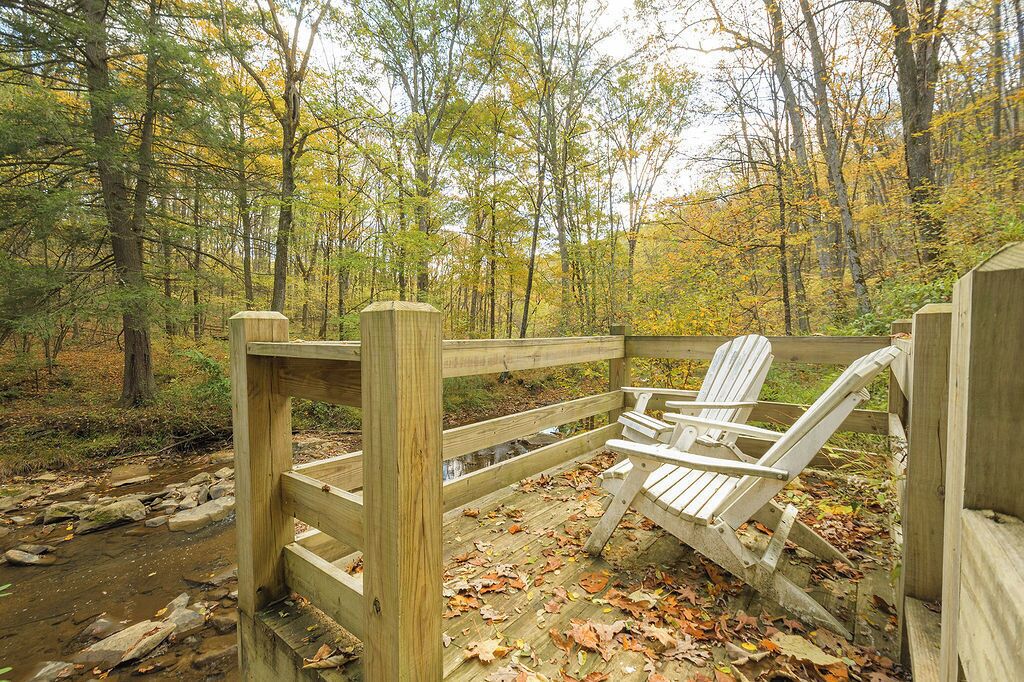 A wooden deck with Adirondack chairs in a forested area.