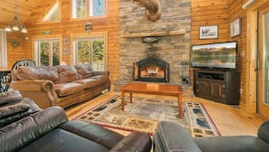 Interior acogedor de una cabaña con chimenea de piedra, mobiliario de cuero y televisor.