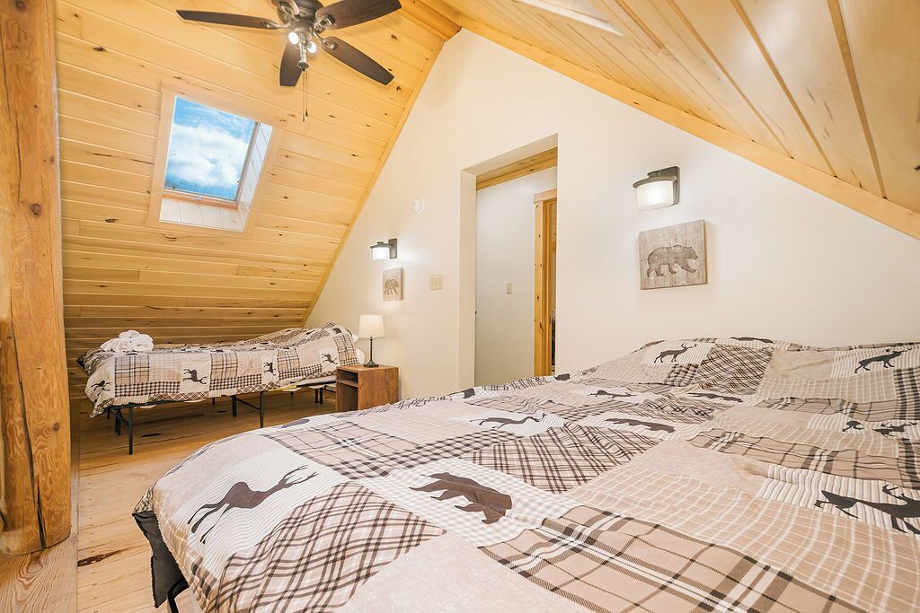 Une chambre confortable avec un grand lit, un plus petit lit en arrière-plan, un ventilateur de plafond et une lucarne.