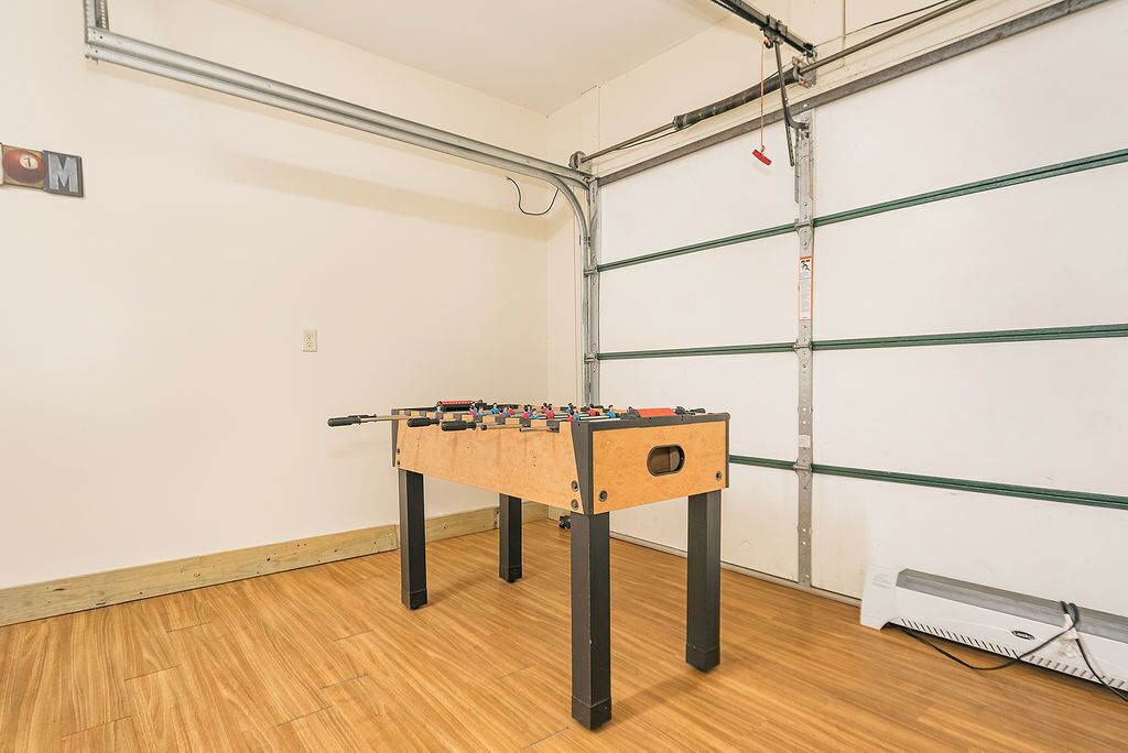 A room with a wooden floor, a foosball table, and a garage door in the background.