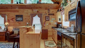 Eine Holzhütte mit Innenausstattung aus Holz, einer Küche inklusive Kühlschrank, Herd und Spüle sowie einem Essbereich mit Tisch und Stühlen.