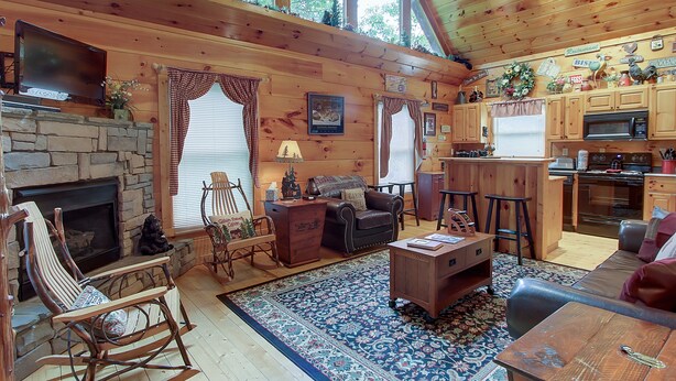 Ein gemütliches Blockhauss-Interieur mit Kamin aus Stein, Holzmöbeln, einer Küchenzeile und großen Fenstern.