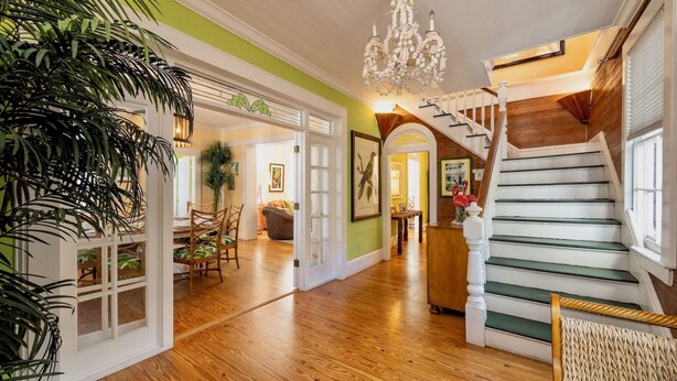 Un hall spacieux doté d’un parquet en bois, d’un escalier aux marches vertes et d’un lustre.