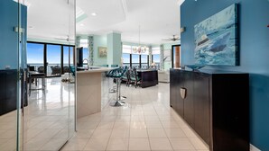 Un hall d’hôtel moderne doté d’une cloison en verre, d’un comptoir d’accueil, d’un espace salon et d’une grande fenêtre offrant une vue sur la mer.