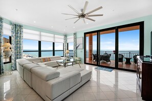 A modern living room with a large sofa, a glass coffee table, and a ceiling fan. - Penthouse in Paradise Gulf with a magnificent view! (Orange Beach)