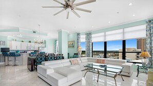 Un vaste espace de vie comprenant un canapé blanc, une table basse en verre et un coin repas avec une table haute et des chaises.