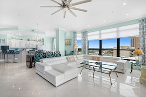 A spacious living area with a white sofa, a glass coffee table, and a dining area with a high table and chairs. - Penthouse in Paradise Gulf with a magnificent view! (Orange Beach)