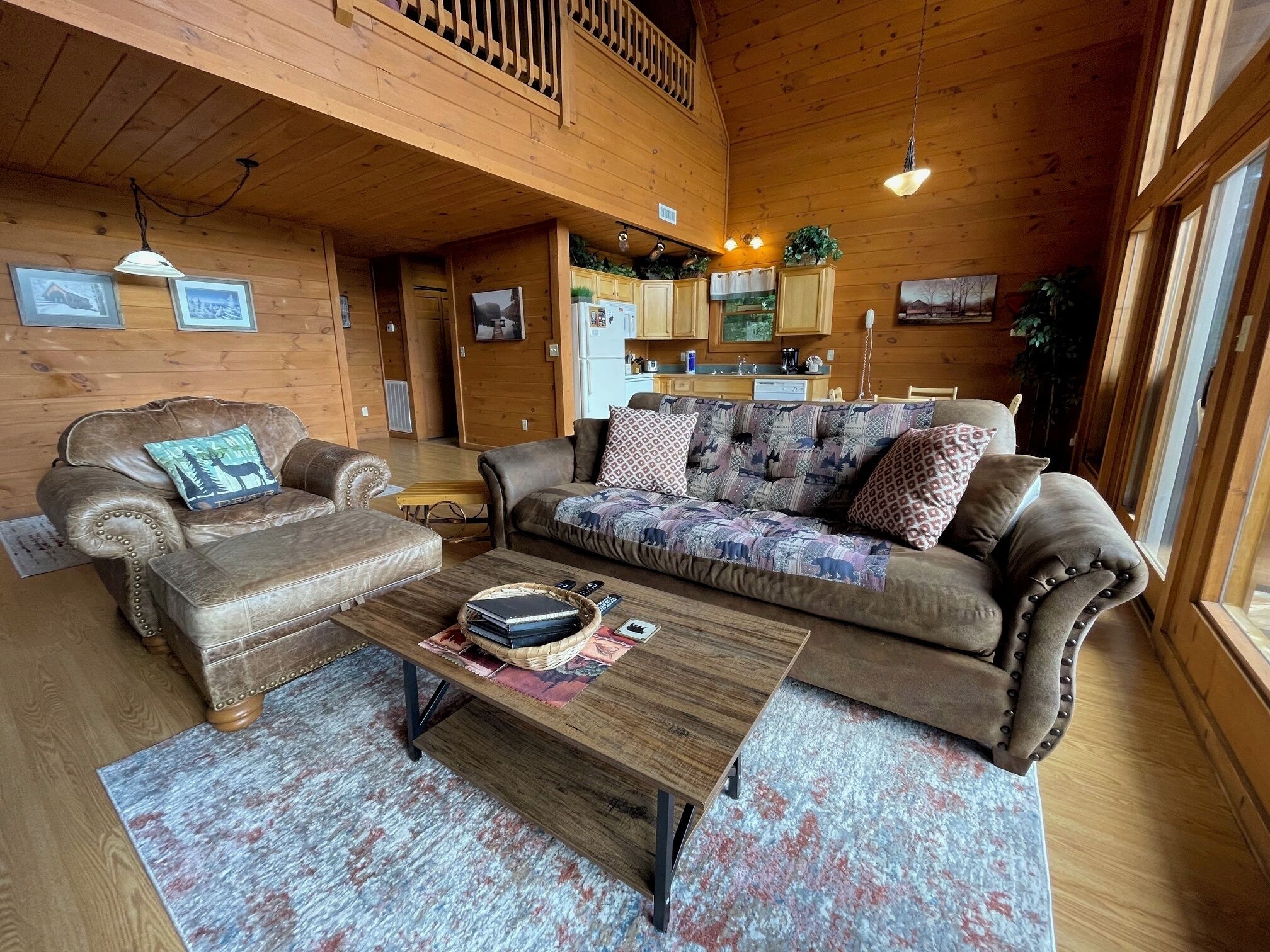A cozy wooden cabin interior with two leather sofas, a wooden coffee table, and a kitchen area in the background.