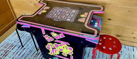 A pinball machine with vibrant graphics and a red stool beside it.