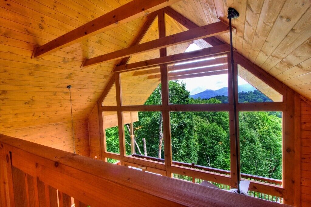 Un interior de madera con un ventanal grande que muestra un paisaje montañoso y boscoso.