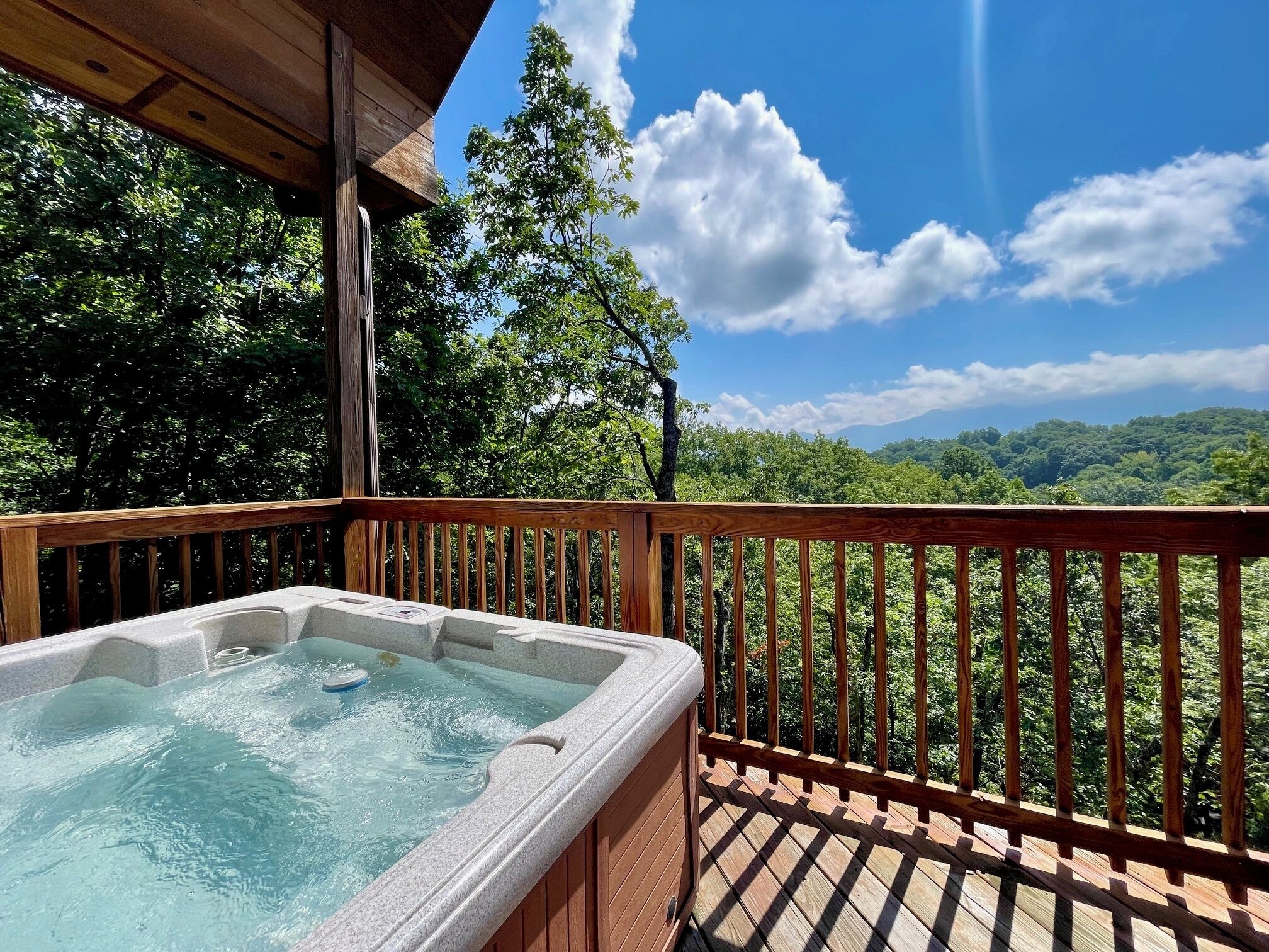 Un jacuzzi en una terraza de madera con vistas a un bosque y montañas.