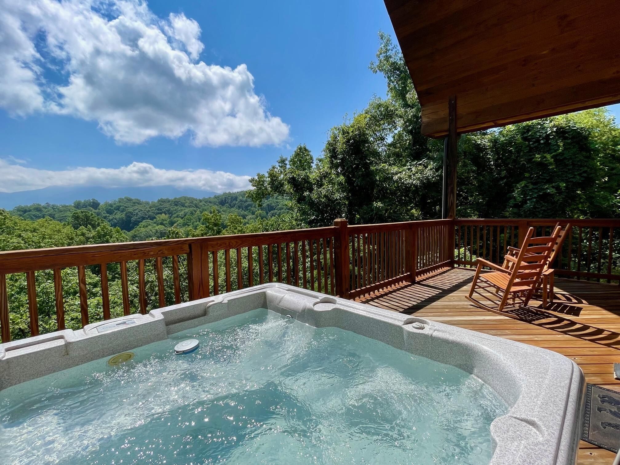 Un bain à remous sur une terrasse en bois, avec vue sur un paysage boisé.