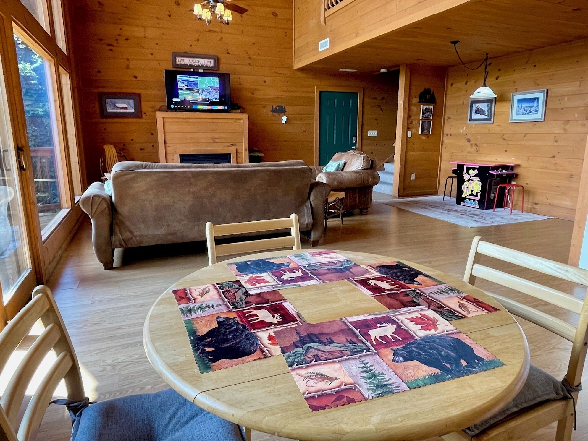 Una habitación acogedora con detalles de madera, una mesa redonda con colcha, un sofá y un televisor sobre un mueble de madera.