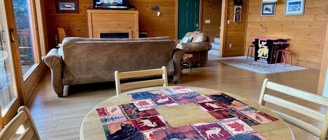 Una habitación acogedora con detalles de madera, una mesa redonda con colcha, un sofá y un televisor sobre un mueble de madera.