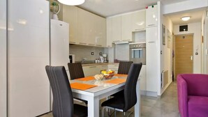 Una cocina moderna con armarios blancos, una mesa de comedor con cuatro sillas y un sillón morado.