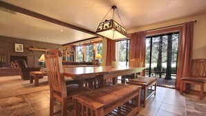 Un vaste espace dédié à la salle à manger, avec une table et des bancs en bois, une cheminée en briques et de grandes fenêtres offrant une vue sur l’extérieur.