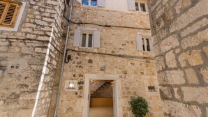 A narrow stone building with a staircase leading to an upper floor. There are windows with shutters and a small potted plant on the ground floor. - Casa Sepia in Trogir old town for up to 6 people (Trogir)
