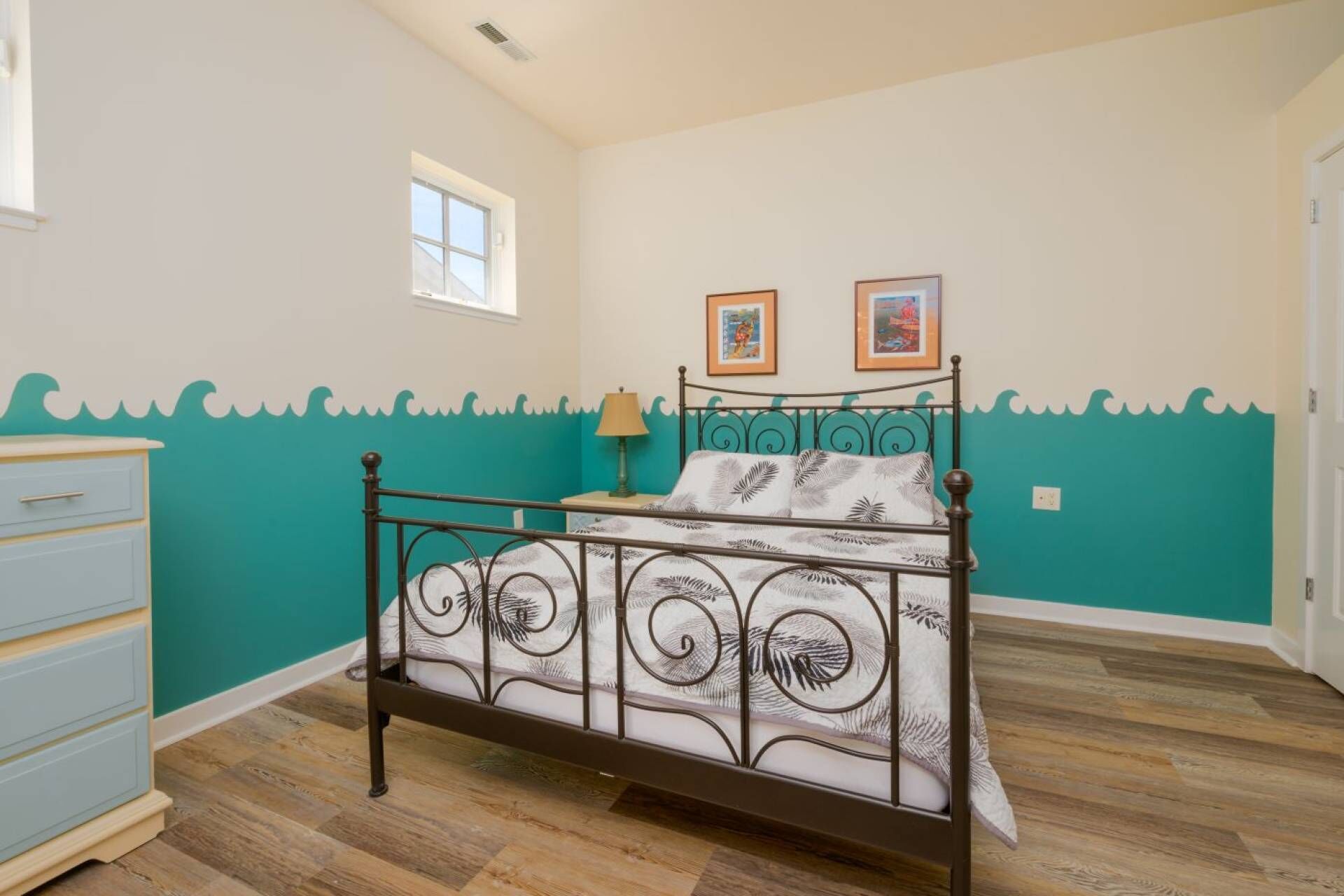 Une chambre à coucher avec un lit, une commode et deux tableaux encadrés accrochés au mur.