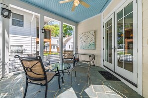 Un patio couvert avec un sol en pierre, des chaises en métal, une table et un ventilateur de plafond.