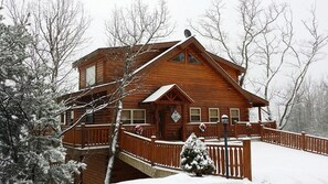 A wooden cabin with a balcony, surrounded by snow-covered trees.