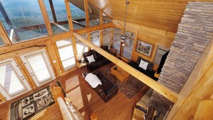 Uma cabana de madeira com quarto no mezanino, sala de estar com lareira e vista para as montanhas.