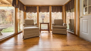 A cozy room with two armchairs, a small table, and large windows with curtains.