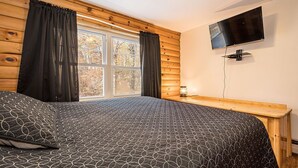 A bedroom with a bed, a TV mounted on the wall, and a window with curtains.