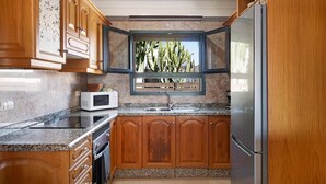 Eine Küche mit Holzschränken, einer Granit-Arbeitsplatte, einer Mikrowelle, einem Spülbecken und einem Kühlschrank.