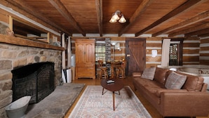 Ein Blockhaushaus-Interieur mit Kamin aus Stein, Holzbalken an der Decke, einem braunen Ledersofa und einem gemusterten Teppich.
