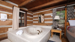 Ein rustikales Zimmer im Chalet-Stil mit einer großen Badewanne, einem hölzernen Bett und einem kleinen Tisch mit einer Lampe.