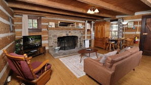 Ein gemütliches Blockhaus-Interieur mit Kamin aus Stein, Holzmöbeln und einem Fernseher.