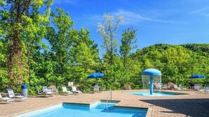 A pool area with lounge chairs and umbrellas, surrounded by trees and a clear sky. - 5BR in Gatlinburg with hot tub and pool table! 1 free ticket to Dollywood! (Gatlinburg)