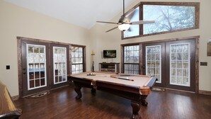 A spacious room with a pool table, large windows, and a ceiling fan. - 5BR in Gatlinburg with hot tub and pool table! 1 free ticket to Dollywood! (Gatlinburg)