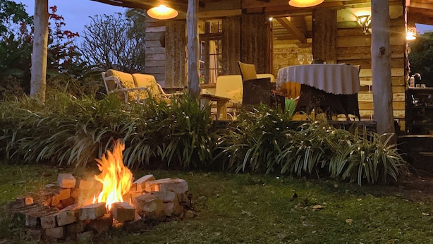 A rustic outdoor seating area with a fire pit, wooden tables, and chairs under a covered roof. - Le Cabanon, perfect for nature lovers (Le Morne)