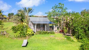 A house with a covered porch, surrounded by lush greenery and a clear blue sky. - Le Cabanon, perfect for nature lovers (Le Morne)