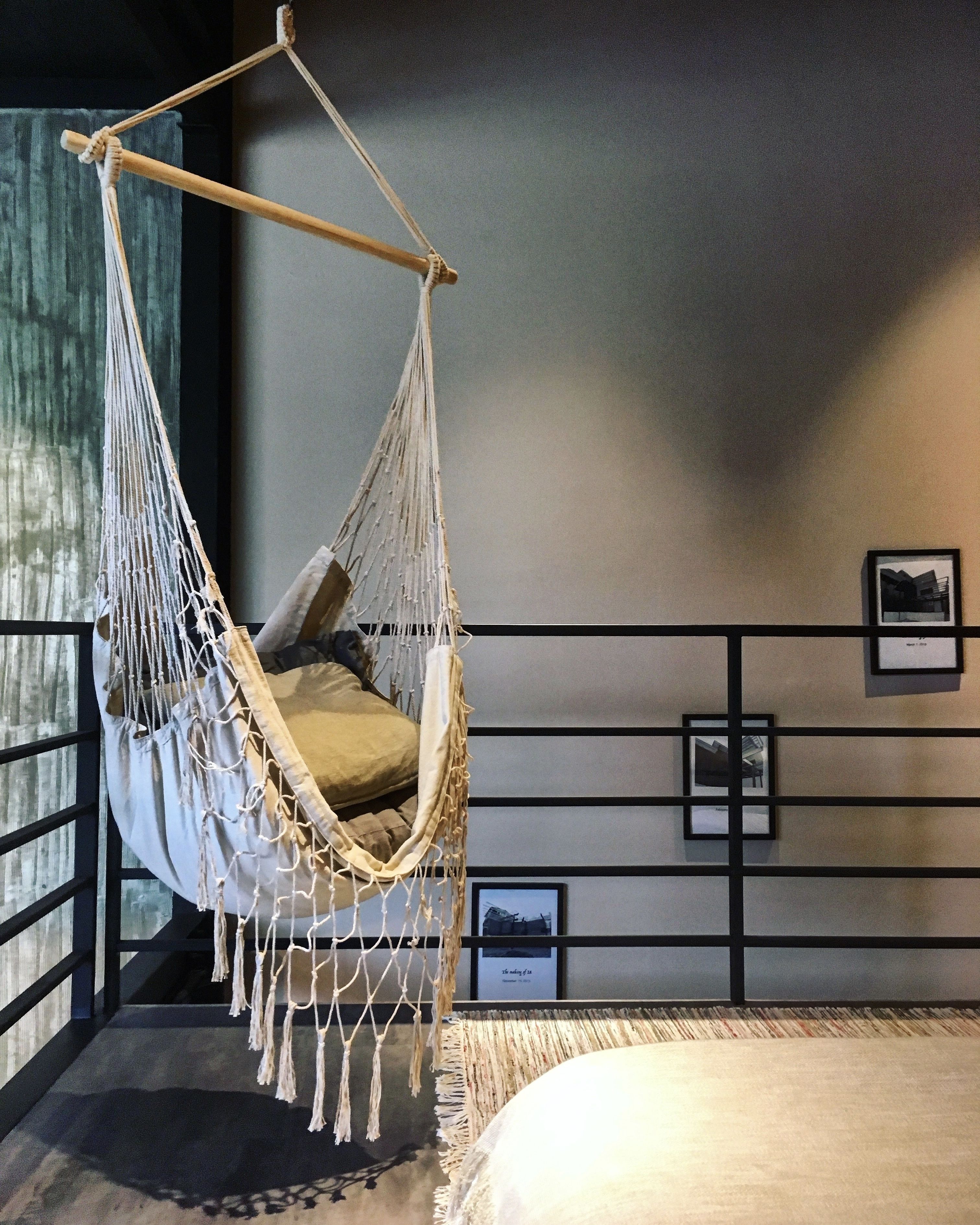 A room with a hanging hammock chair, a bed, a framed picture on the wall, and a small rug on the floor.