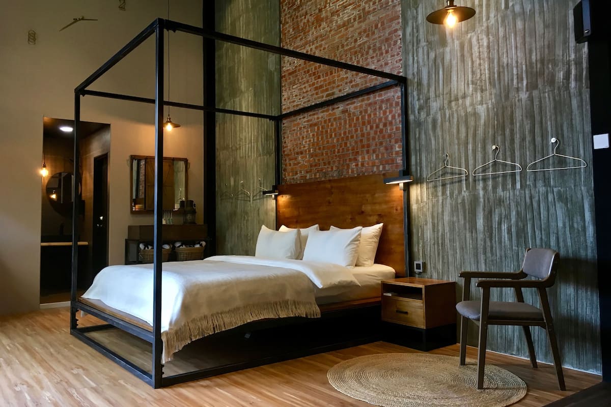 A modern bedroom with a four-poster bed, wooden nightstands, a round woven rug, and a brick-patterned wall.