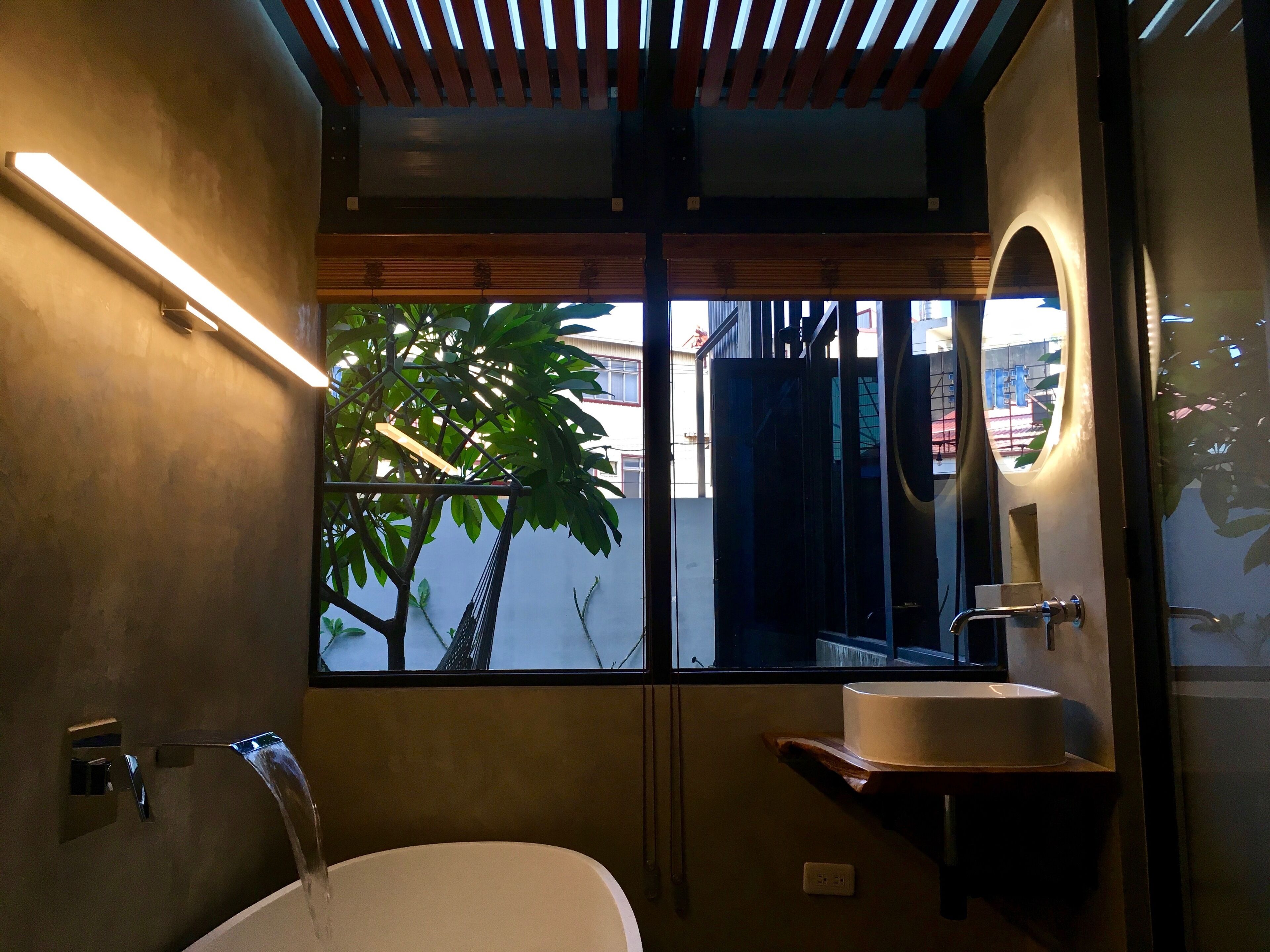A modern bathroom with a bathtub, a sink, and a window with a view of a tree and buildings.