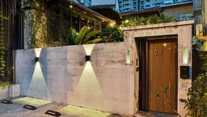A hotel entrance with a concrete wall, a wooden door labeled "28", and a small garden area with plants and a thatched roof structure. - 28 The Loft (Tainan)
