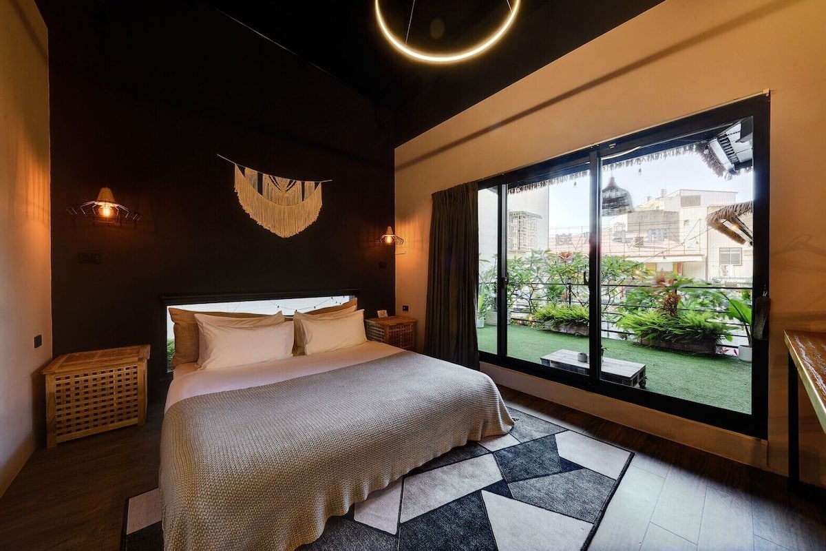 A modern bedroom with a large bed, a view of greenery outside, and a unique ceiling light.