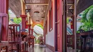 A corridor with wooden chairs and tables, a tiled floor, and a glass door leading outside. - Kata Leaf Resort (Karon)