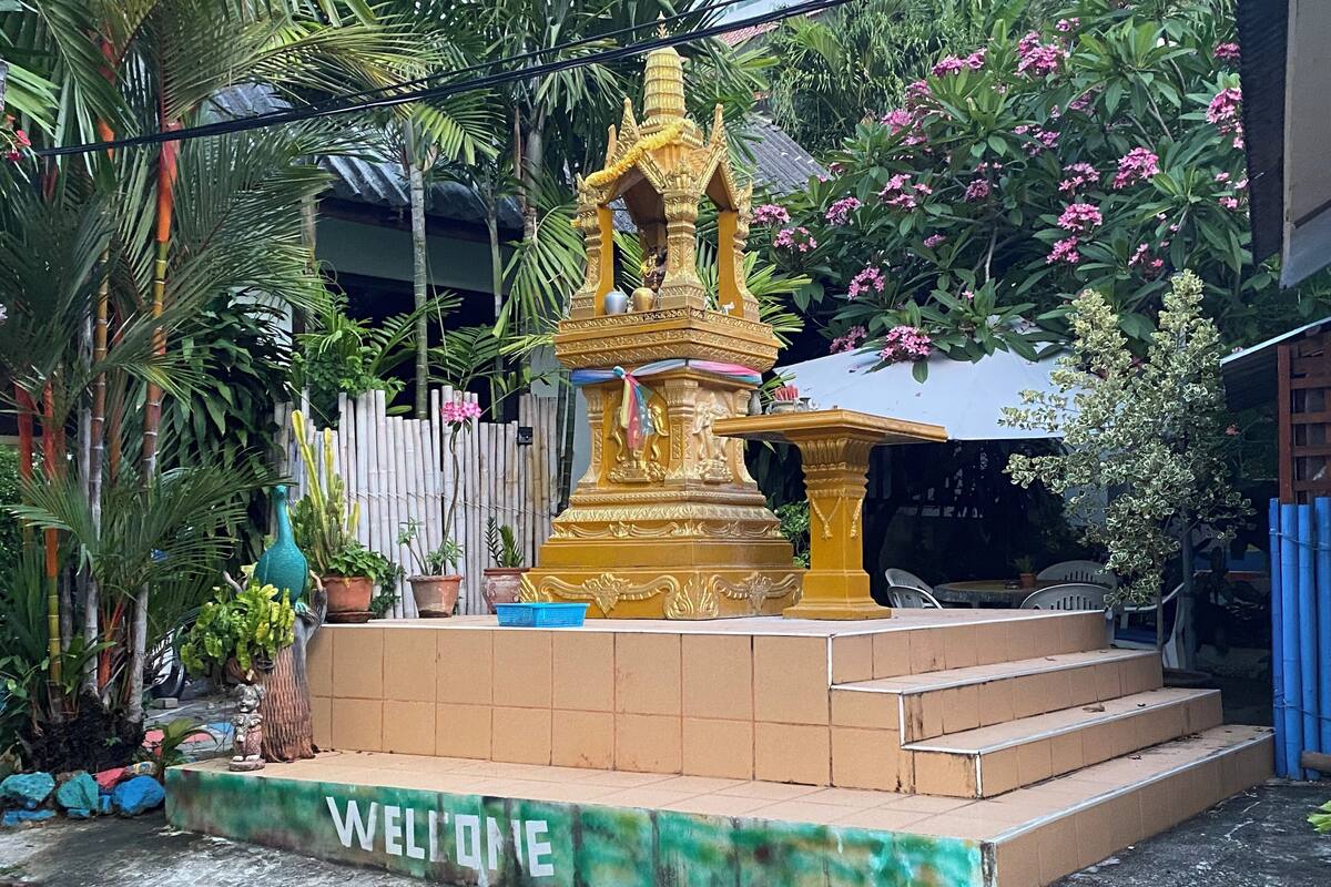 Eine goldene Statue mit Sockel und Stufen, umgeben von Topfpflanzen und einem 'WELCOME'-Schild.