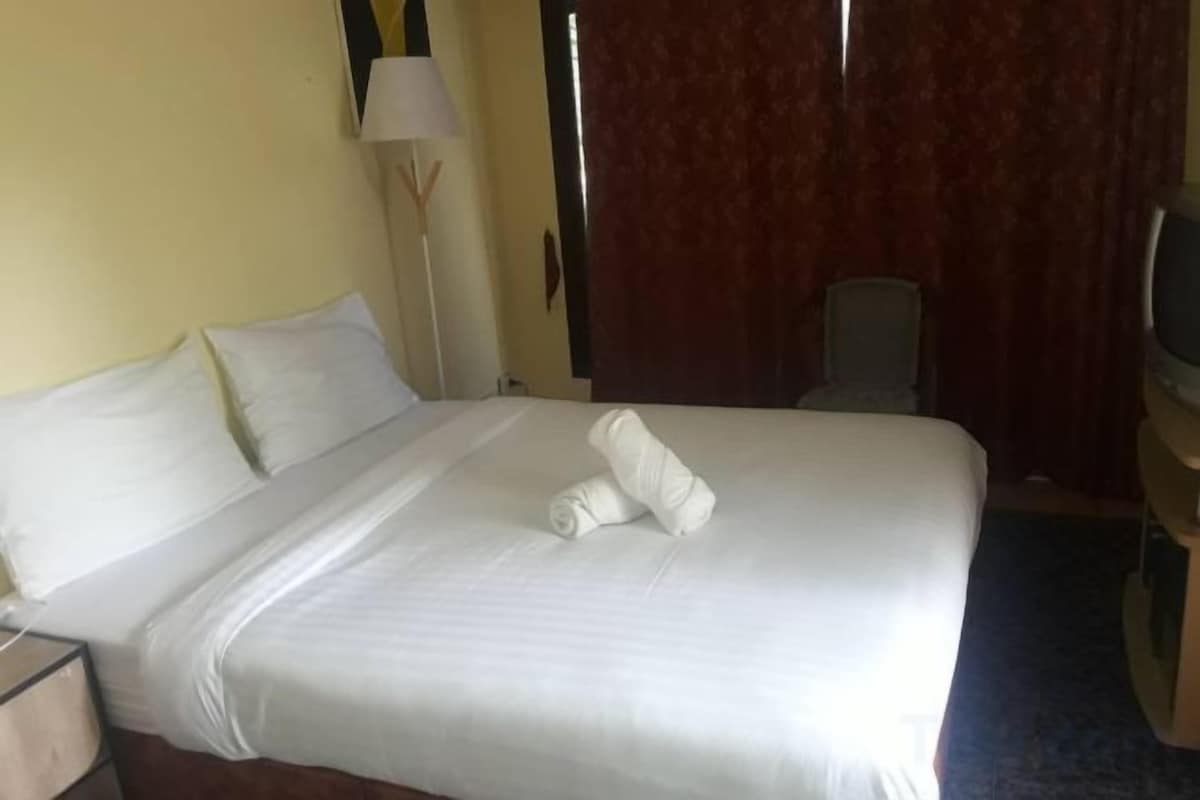 A hotel room with a large bed, a desk, a chair, a lamp, and a television.