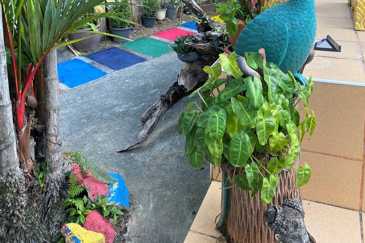Ein tropischer Garten mit einer Pfauenstatue, Bambuspflanzen und bunten Matten am Boden.