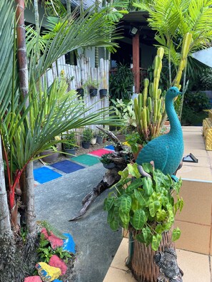A tropical garden with a peacock statue, bamboo plants, and colorful mats on the ground. - Kata Leaf Resort (Karon)