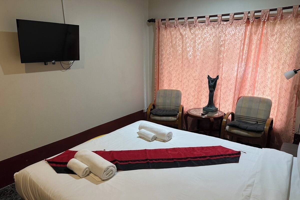 Ein Hotelzimmer mit einem Bett, zwei Sesseln, einem kleinen Tisch, einer Statue und einem an der Wand befestigten Fernseher.