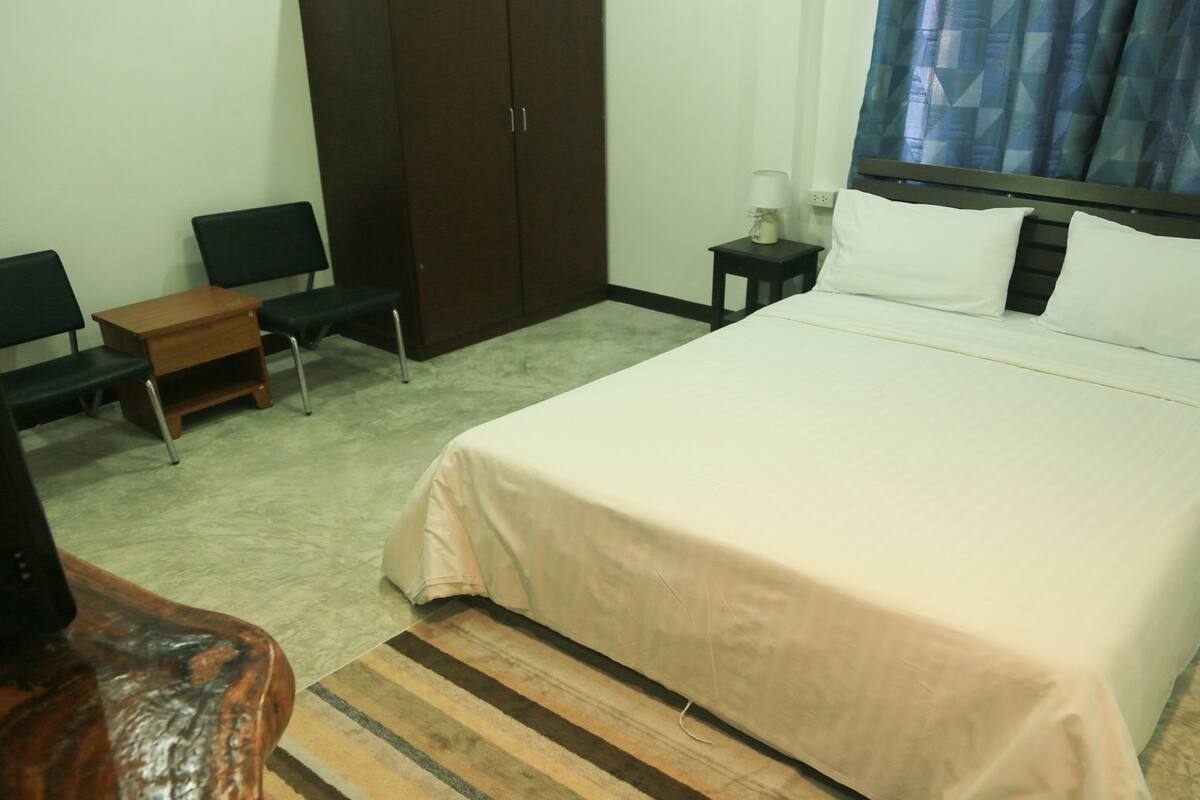 Ein Hotelzimmer mit Bett, Schreibtisch, Stuhl, Kleiderschrank und Nachttisch mit Lampe.
